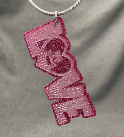 LOVE car charm in glittery pink with the O; shaped like a heart featuring a Jeep inside, with tires touching the heart&#39;s sides.