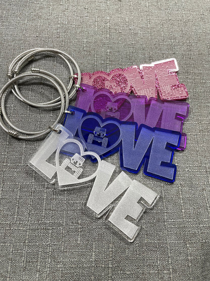 All LOVE car charms laid out in a fan shape, slightly overlaying each other in glitter pink, purple, blue, and white, showcasing their vibrant colors.