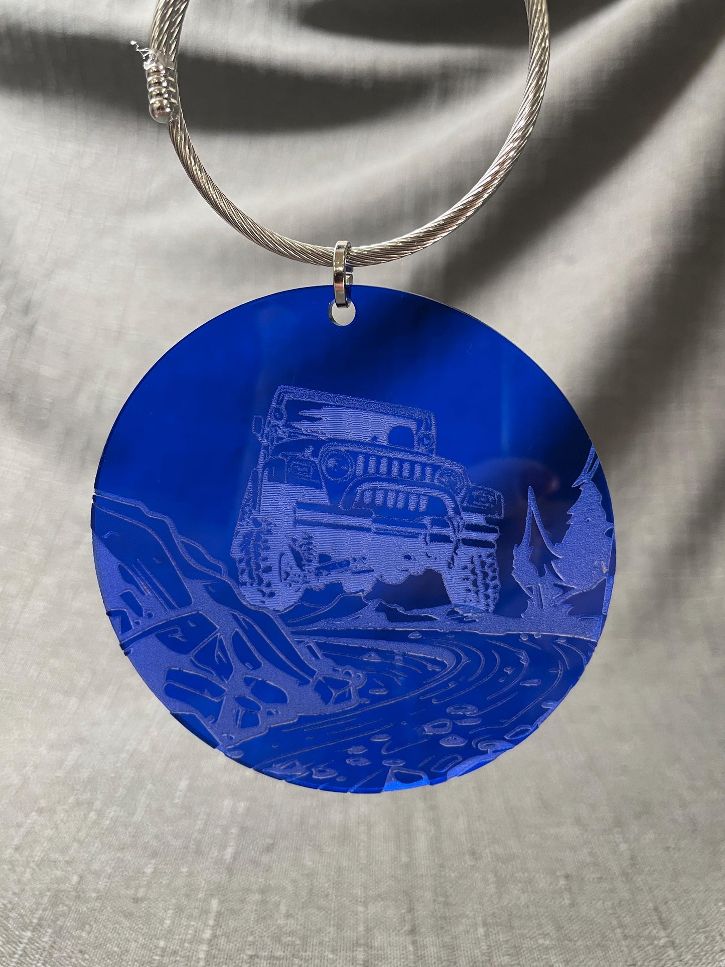 Adventure car charm with Jeep engraving, hanging on a blue background, ideal for off-road enthusiasts.