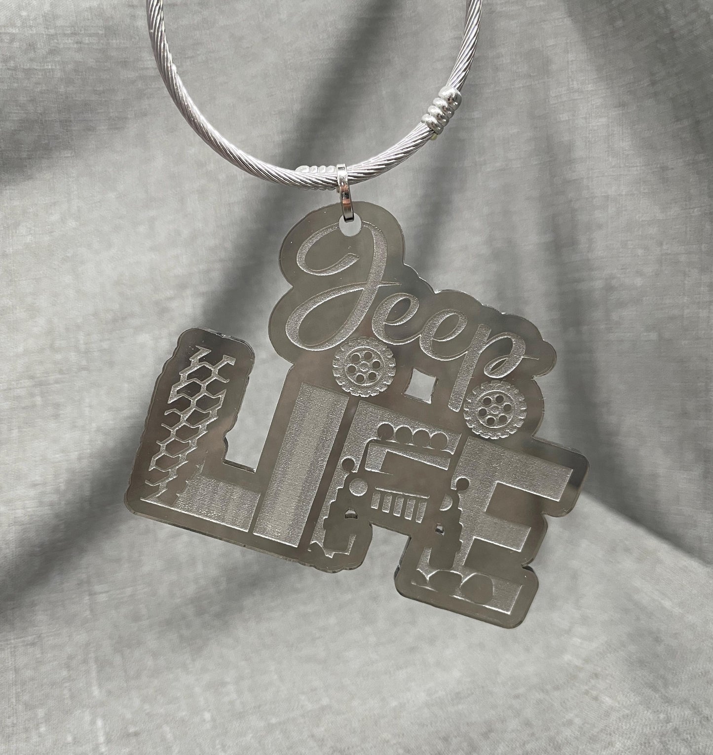 Smoke gray Jeep car charm displaying the word JEEP with Jeep tires beneath, the word LIFE next to tire tracks, and an off-roading Jeep approaching the viewer.