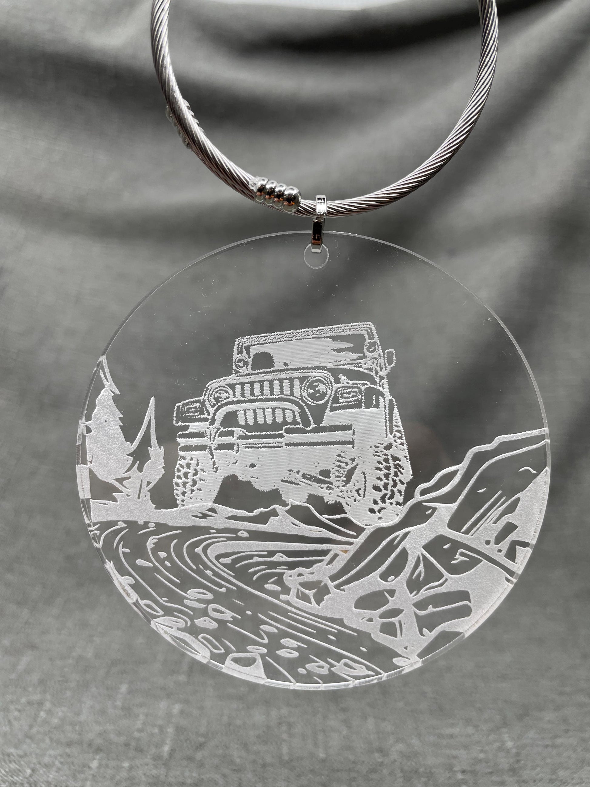 Hanging Adventure car charm with a Jeep in a river bed design on a clear background, smoky engraved look