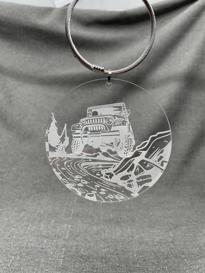 Hanging Adventure car charm with a Jeep in a river bed design on a clear background, smoky engraved look.