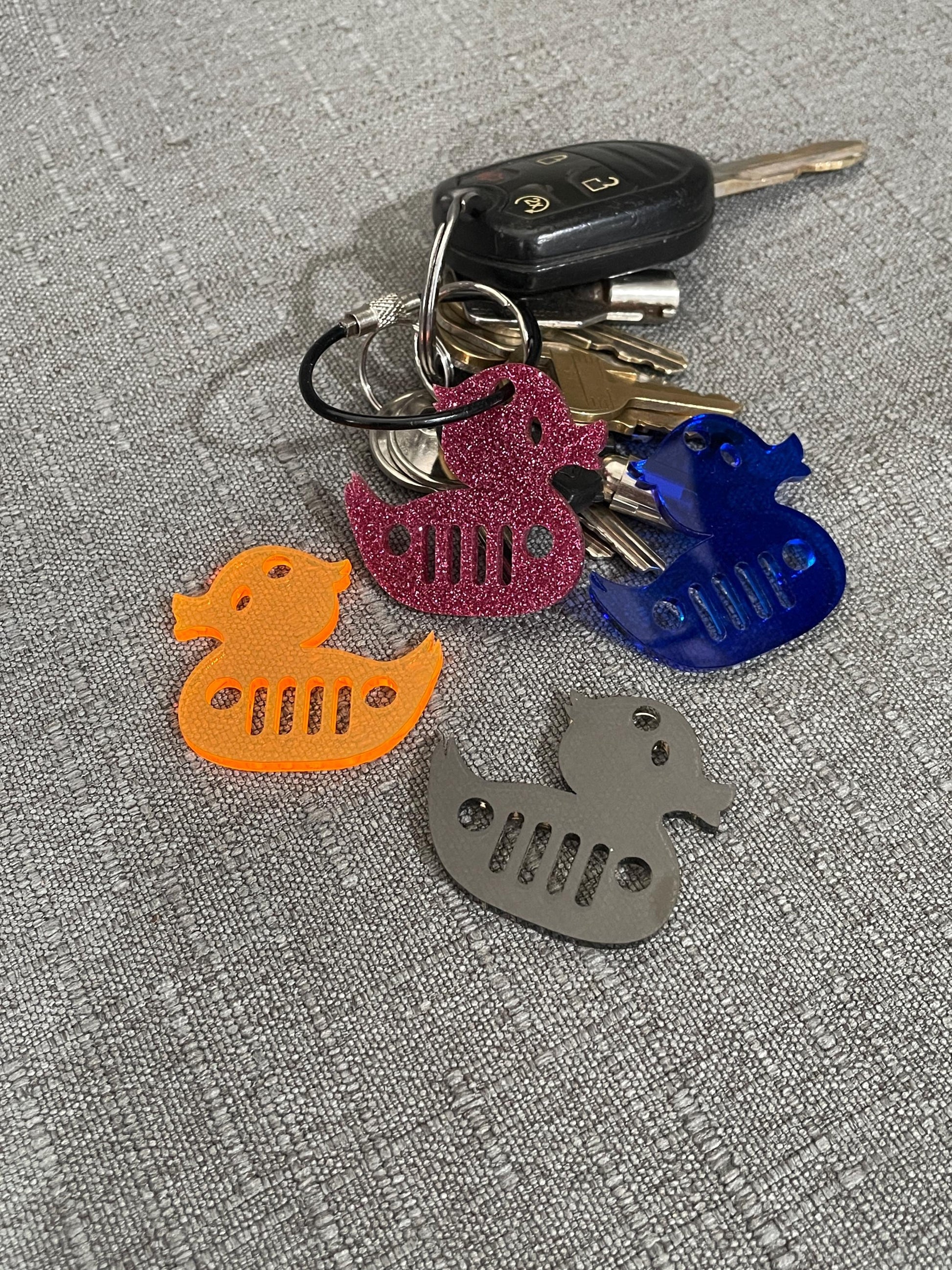 Glitter pink, blue, orange, and smoke gray mini duck key chains on and around a set of keys, showcasing color choices for Jeep fans.